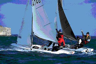 Two small sailboats race side by side on choppy blue water, with sailors leaning outward to balance. One person gestures upwards. A rocky coastline is visible in the background.