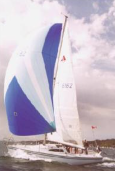 A sailboat with large white and blue sails glides across the water under a partly cloudy sky, with several people visible aboard.