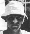 Black and white photo of a person wearing a light-colored bucket hat, facing the camera and smiling slightly, with a blurred outdoor background.
