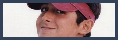 A young person wearing a maroon cap looks at the camera with a slight smile, set against a plain light background and framed by a dark blue border.