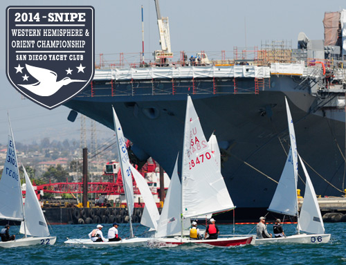 Small sailboats race in front of a large gray naval ship at the 2014 Snipe Western Hemisphere & Orient Championship, hosted by the San Diego Yacht Club, as seen in the event logo on the top left.