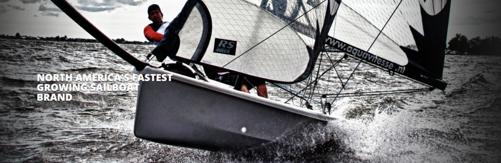 A person sails a small racing sailboat at high speed on choppy water, with water spraying up. Text on the image reads: “North America’s fastest growing sailboat brand.”.