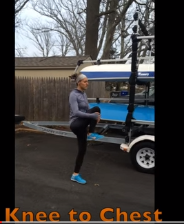 A person in athletic clothing stands outdoors, pulling one knee up toward their chest as a stretch. A trailer with a boat is visible in the background. The text 'Knee to Chest' appears at the bottom of the image.