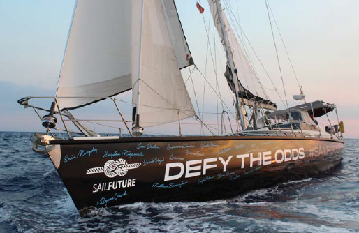 A large sailing yacht named “SailFuture” sails on the open sea at sunset, displaying the phrase “DEFY THE ODDS” in bold letters on its hull, along with signatures and a rope knot graphic.