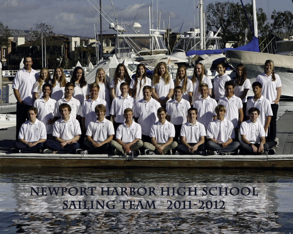 A group of students in white shirts pose on a dock in front of boats for the Newport Harbor High School Sailing Team photo, 2011–2012. The team is seated and standing in rows, with a marina and water in the background.