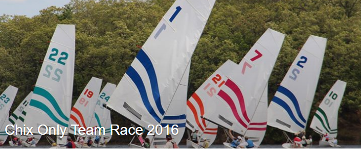 A row of sailboats with colorful striped sails, each displaying a large number, race closely together near the shore; text reads “Chix Only Team Race 2016.”.