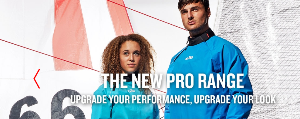Two people wearing blue sailing jackets stand in front of a sailboat sail. Bold text reads 'The New Pro Range. Upgrade your performance, upgrade your look.' Red and white sail and netting are visible in the background.