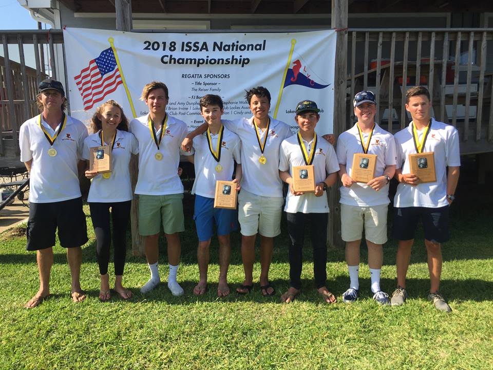 Eight young adults in white shirts and medals stand in a row on grass, holding plaques, in front of a banner reading '2018 ISSA National Championship' with American and sailing flags.