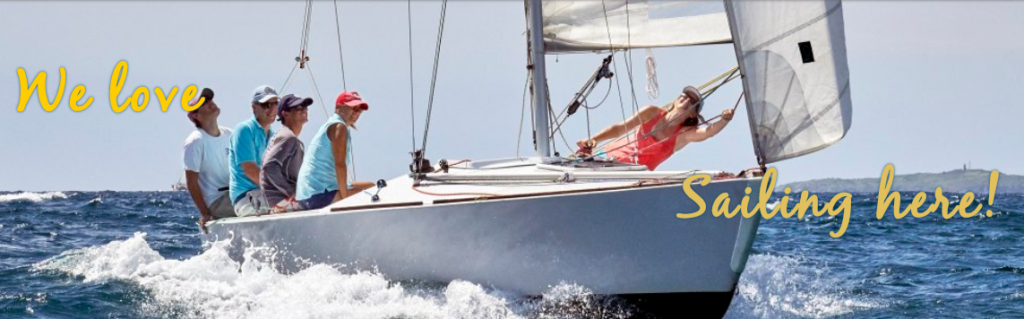 Five people are sailing a white sailboat on open water under a sunny sky. The text on the image reads, "We love Sailing here!" in yellow script.