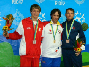 Three male athletes wearing medals and holding flowers stand on a podium in front of a blue Rio 2007 backdrop. They appear to be celebrating after a sports competition.