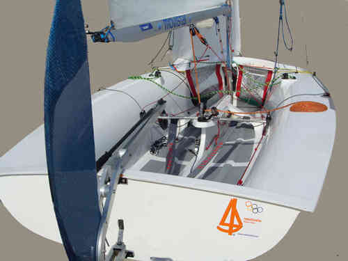 Close-up view of a small racing sailboat cockpit, featuring various ropes, lines, and controls. Olympic and sailing class logos are visible on the hull. The background is neutral and uncluttered.