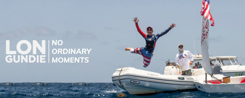 A man in patriotic USA-themed clothing jumps joyfully off a small boat into the ocean, while another person on the boat smiles. Behind them, a larger boat displays American flags. Text reads, "LON GUNDIE | NO ORDINARY MOMENTS.