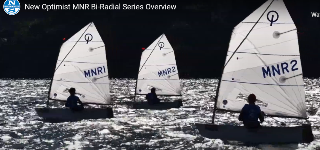 Three small sailboats with "MNR1" and "MNR2" on their sails glide across a sunlit, rippling body of water, with silhouetted sailors steering each boat.