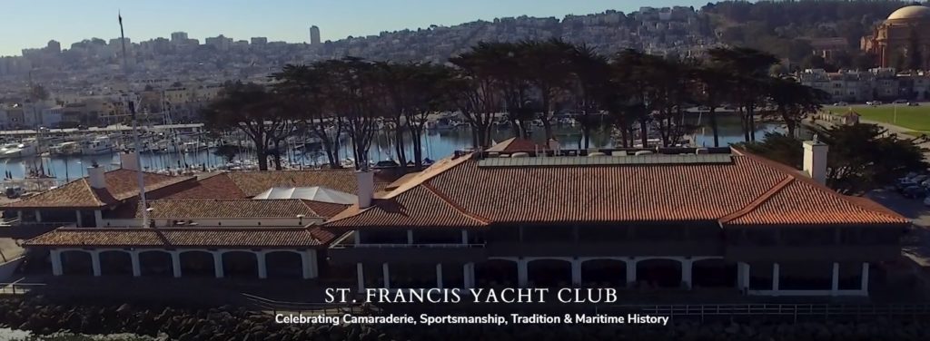 Aerial view of the St. Francis Yacht Club with its red-tiled roof, waterfront marina, and boats docked, against a backdrop of trees and a cityscape. Text reads: 'St. Francis Yacht Club.