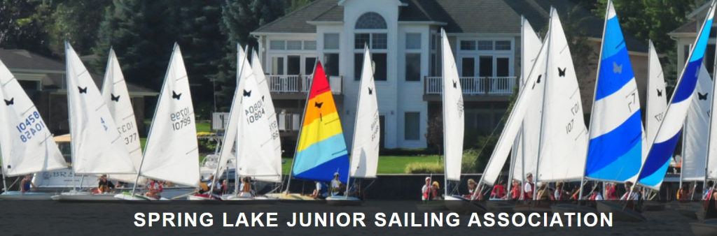 A group of small sailboats with colorful sails are gathered on a lake in front of lakeside houses; text at the bottom reads 'Spring Lake Junior Sailing Association.