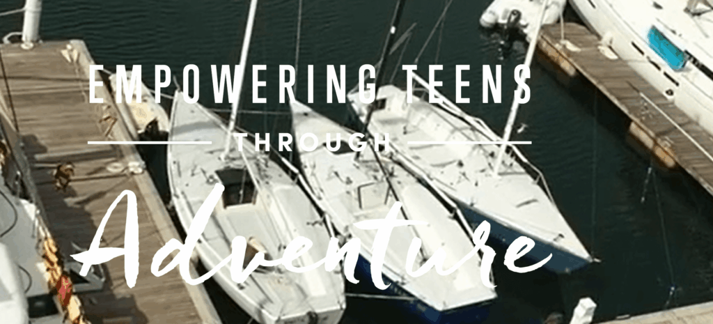 Three docked sailboats seen from above, with the text 'Empowering Teens Through Adventure' overlaid on the image. The boats are tied to wooden piers in a marina.