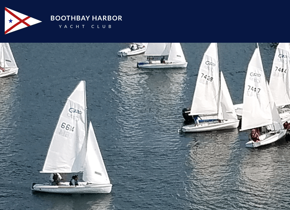 Sailboats with white sails race on the water near Boothbay Harbor Yacht Club, as shown by the club’s logo and banner at the top of the image. Multiple boats are visible, each with people aboard.