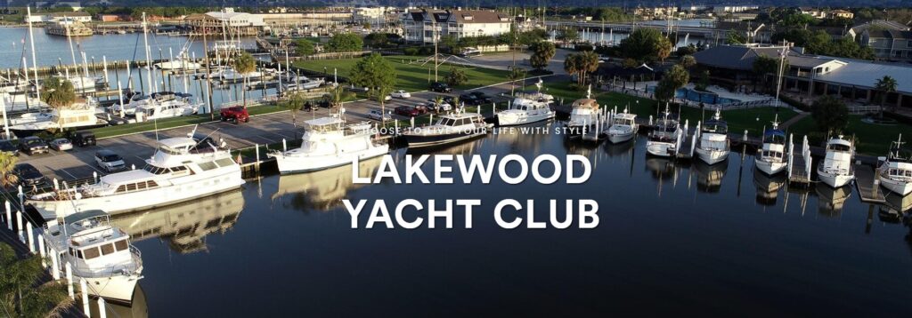 Aerial view of Lakewood Yacht Club marina with several docked yachts, boat slips, green lawns, palm trees, and clubhouse buildings along the waterfront under a clear sky.