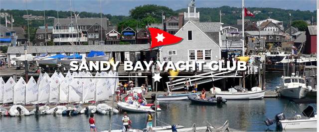 Harbor scene with sailboats docked near a pier, people in small boats and on the dock, buildings in the background, and the text 'Sandy Bay Yacht Club' with a red flag logo overlaid on the image.