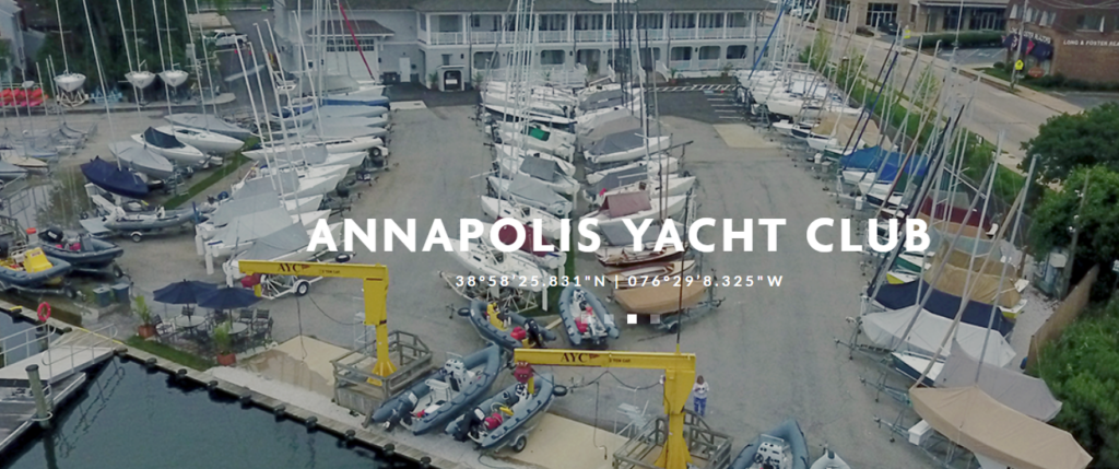 Aerial view of the Annapolis Yacht Club showing multiple sailboats docked and parked on land, club buildings, and yellow cranes, with text displaying the club's coordinates over the image.