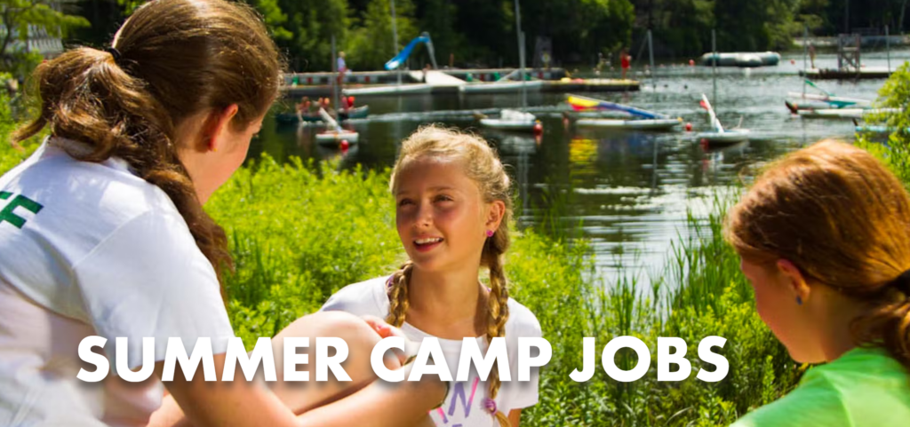 Three young people sit and talk by a lake with sailboats in the background, surrounded by greenery. Text over the image reads “SUMMER CAMP JOBS.”.