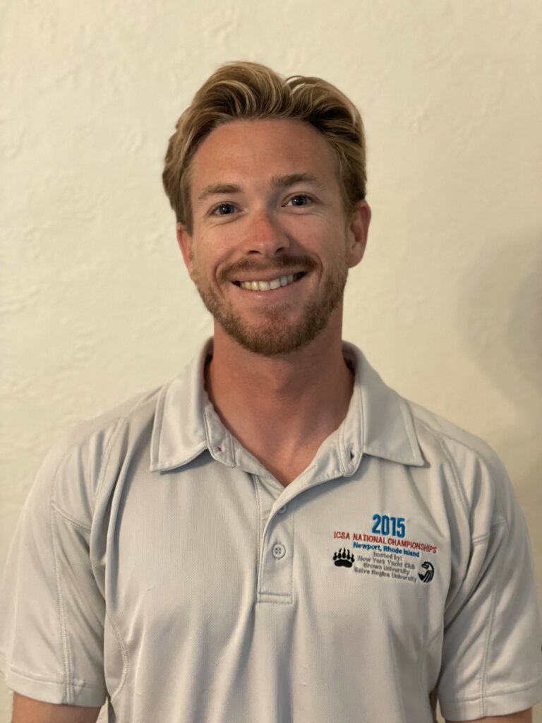 A smiling man with short light brown hair and a beard is wearing a light gray collared shirt with a "2015 ICRA National Championships" logo, standing against an off-white textured wall.