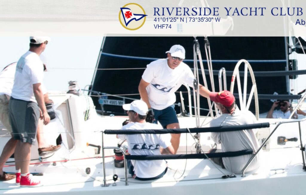 Four people in casual clothes and hats are on a white sailboat, preparing to sail. They are smiling and interacting, with a large black sail in the background. The Riverside Yacht Club logo appears at the top.