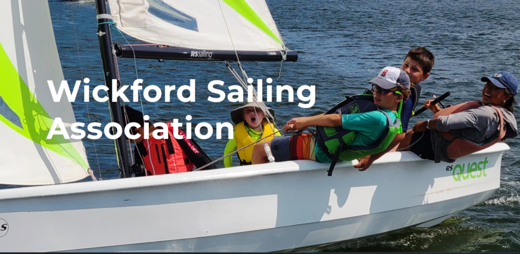 Four kids in life jackets sail a small white sailboat on the water, smiling and laughing. The text 'Wickford Sailing Association' appears over the image.