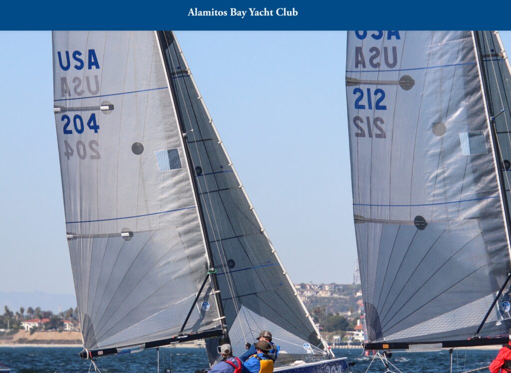 Two sailboats with visible sail numbers '204' and '212' race side by side on the water near Alamitos Bay Yacht Club, with crew members on board and a coastal town visible in the background.