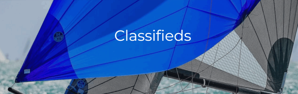 Blue and black sails of racing sailboats with the word "Classifieds" in white text centered over the image. The background shows water and a hint of the horizon.